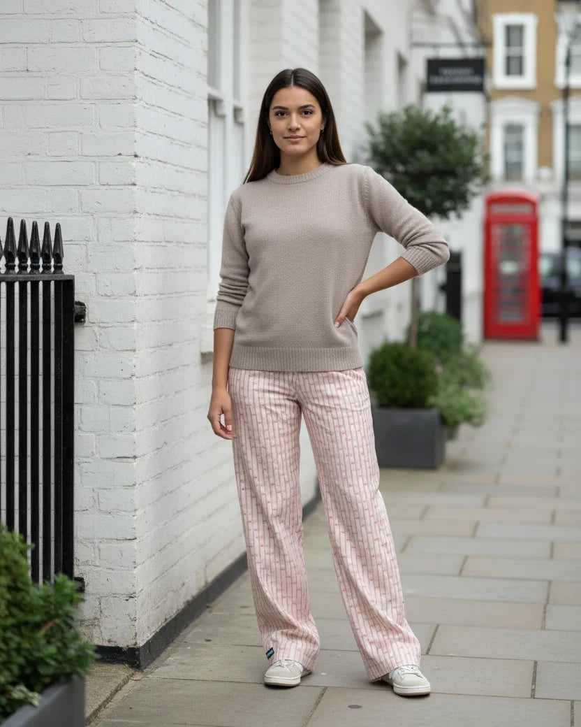 Woman in a beige sweater and pink checkered pants standing on a street with a red phone box in the background.