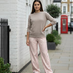 Woman in a beige sweater and pink checkered pants standing on a street with a red phone box in the background.