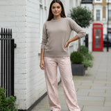 Woman in a beige sweater and pink checkered pants standing on a street with a red phone box in the background.