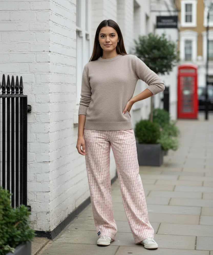 Woman in a beige sweater and pink checkered pants standing on a street with a red phone box in the background.