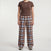 A model wearing a brown short-sleeve t-shirt with a small star logo on the chest and brown plaid lounge pants with blue and beige stripes, standing against a light gray background.